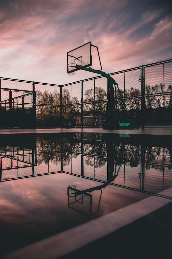 A tranquil view of a basketball court with reflections during sunset, creating a serene urban landscape.